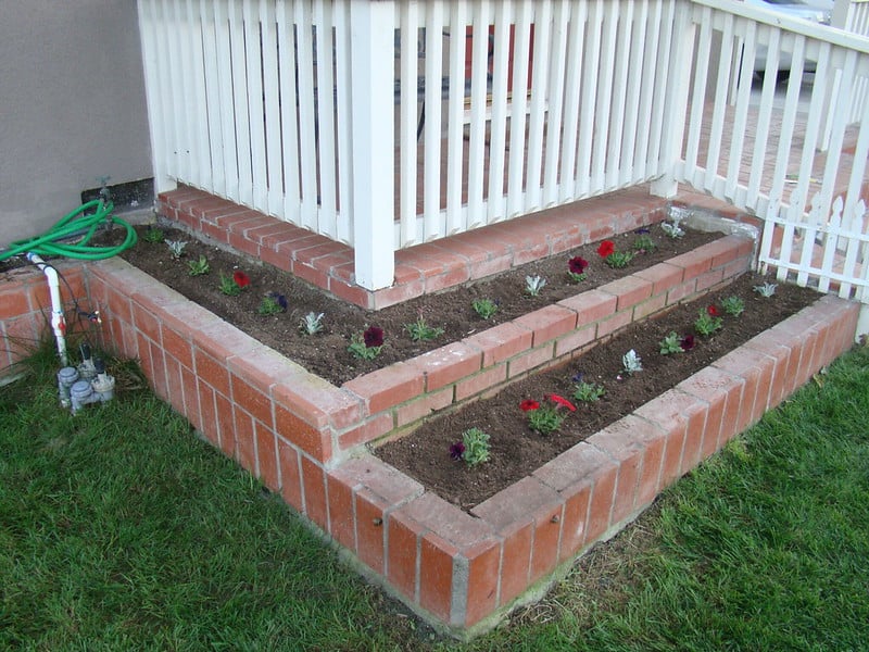Small flowers planted in raised beds around a porch