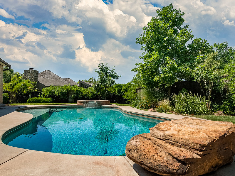 in-gound pool with a large rock in the foreground and trees in the background