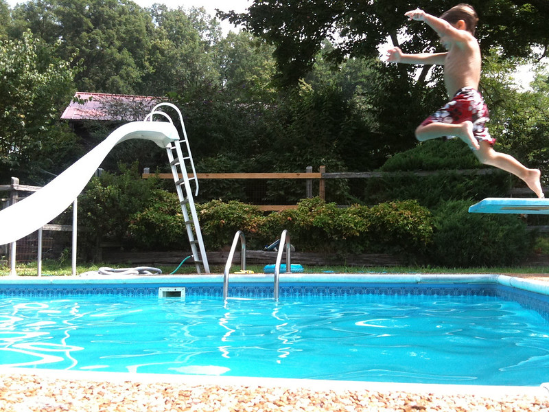 Child jumping off a diving board with a pool slide in the background