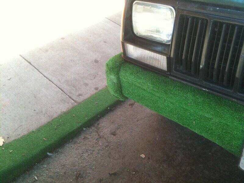 Car bumper and curb of the sidewalk are covered in turf