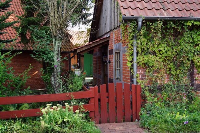 A reddish-brown stained fence and gate on the side of a house with lots of greenery and ivy growing on the brick of the home.