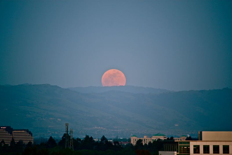A pink supermoon sets behind the mountains near Fremont, casting a rosy glow on the homes and high-rises peaking out of the skyline.