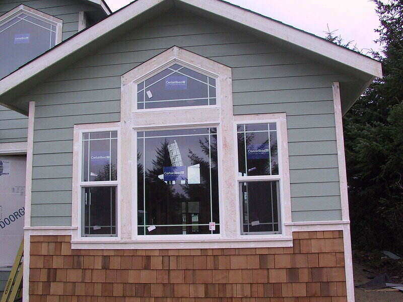 Front portion of a house with colored siding around a window and wood siding below the window