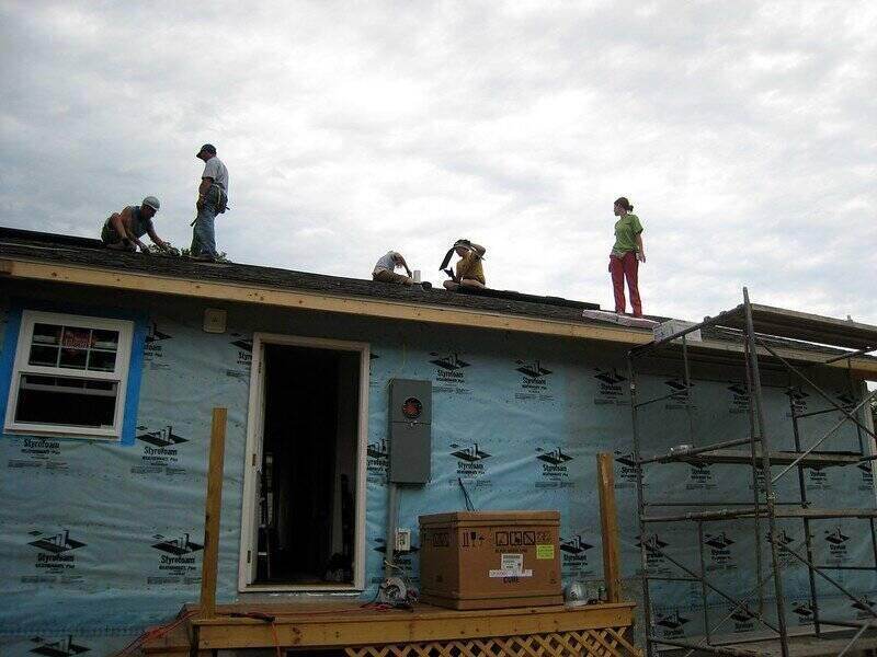Group of people on a roof and look to be putting down asphalt tiles