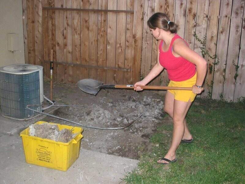 Woman digging out a small concrete pad and removing it