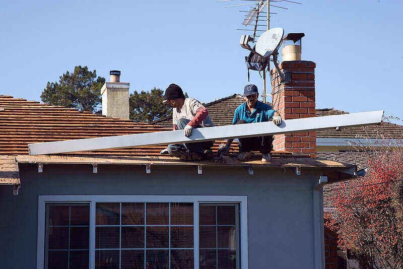 Two men removing gutters from the roof of a house