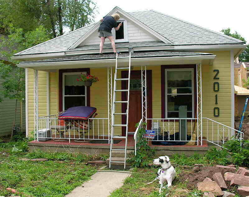 Homeowner painting the very top peak of the house