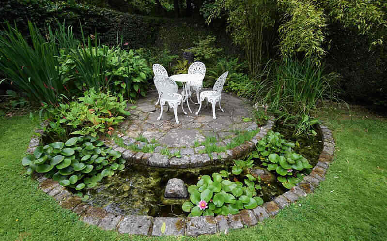 Stone foundation patio, with a small moat and water plants around the perimeter and a table of chairs in the center.