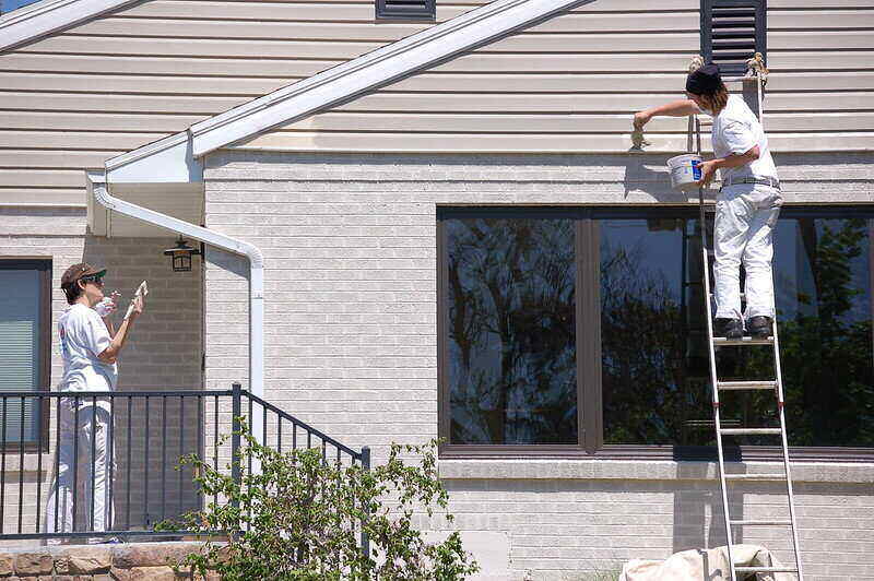 two workers paining the exterior of a house and one is on a ladder