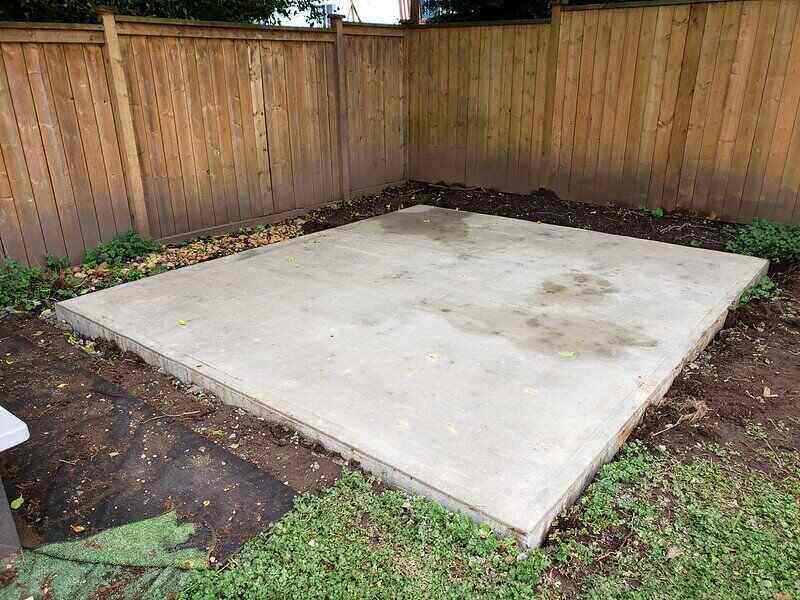 A small concrete slab in the backyard with a fence around two sides of the pad