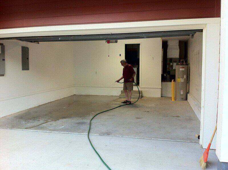 Man using a hose to spray down his concrete garage floor