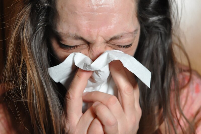Woman holding a tissue to her nose and her eyes are closed