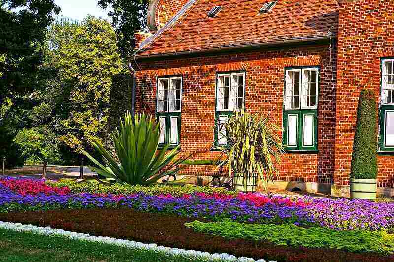 picture of a brick house with a large, colorful flower bed in front of it