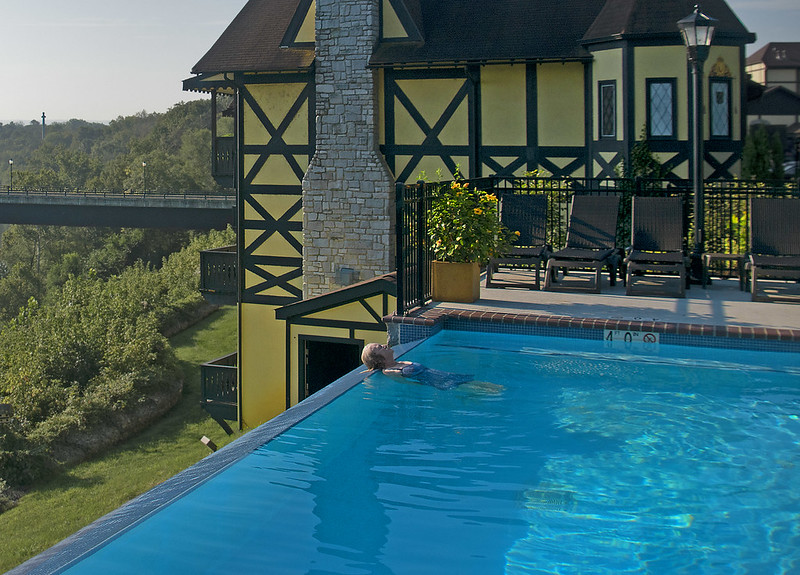 Woman leaning against the side of an infinity pool with a house in the background