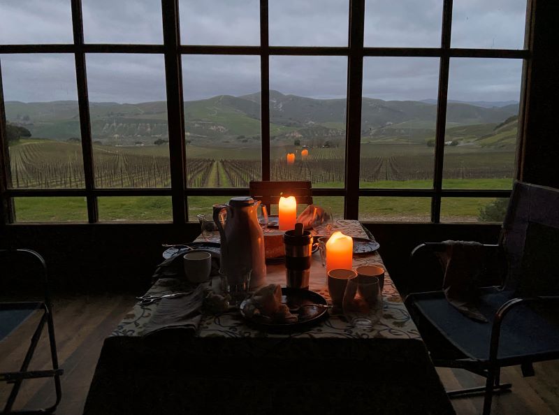 A candlelit dinner table is set up by a large, paned window overlooking the Sanford and Benedict Vineyards, one of the shooting sites in the cult film “Sideways”