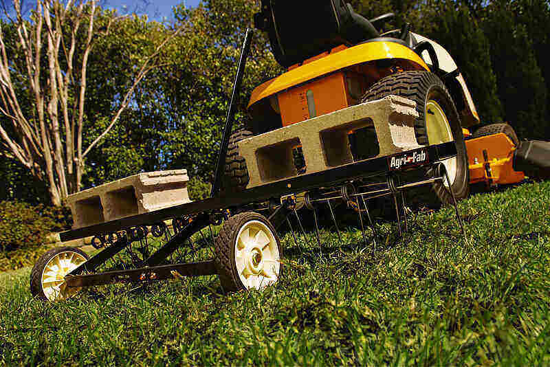 Verticutter being pulled behind a riding lawnmower