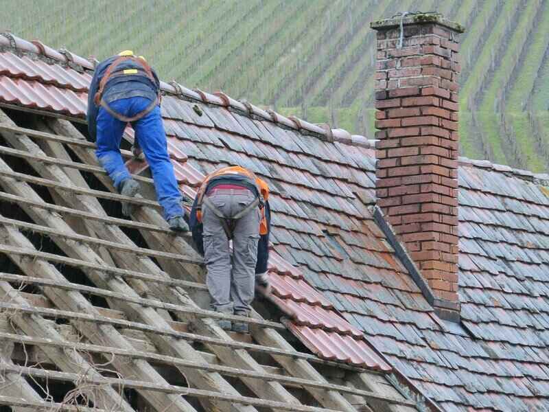 Workers replacing new and different material shingles to a roof