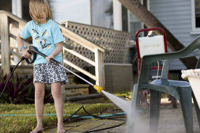 Child using a pressure washer on a plastic lawn chair