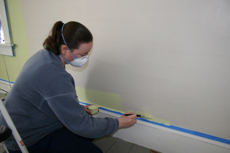 Woman using a small brush to paint along the edge of the baseboard in a room