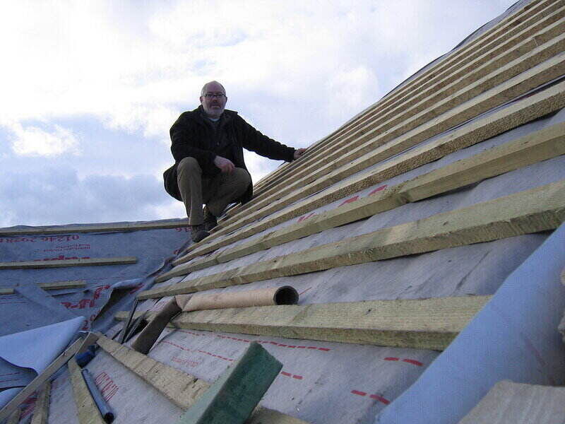 Man sitting on top of a roof that is in the middle of being replaced