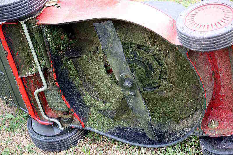 Underside of a used lawn mower with grass clippings around the inside and the blade