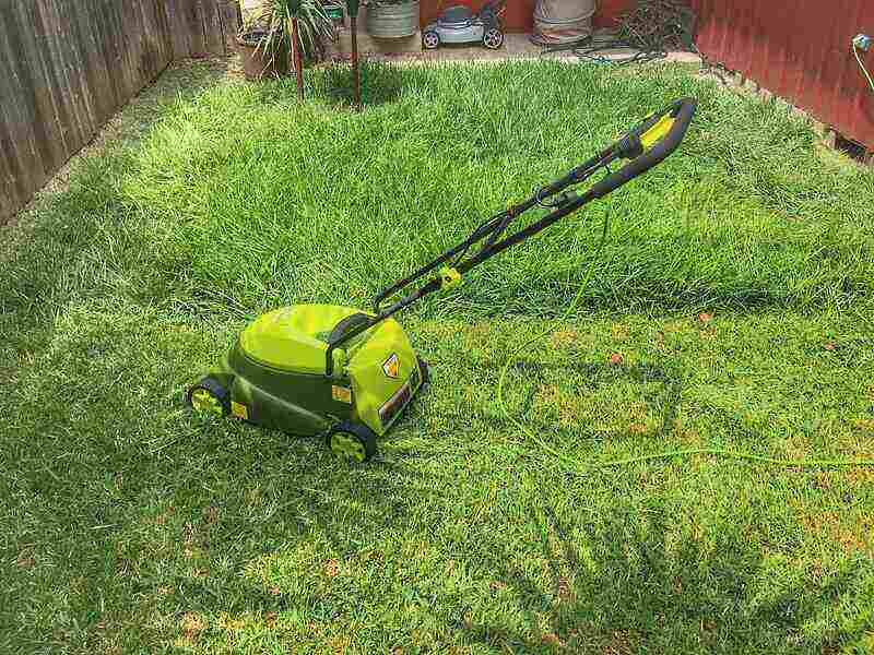 Green electric mower sitting with half the lawn mowed