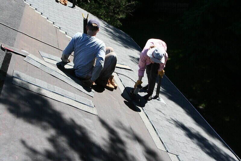 2 workers on a roof replacing the shingles