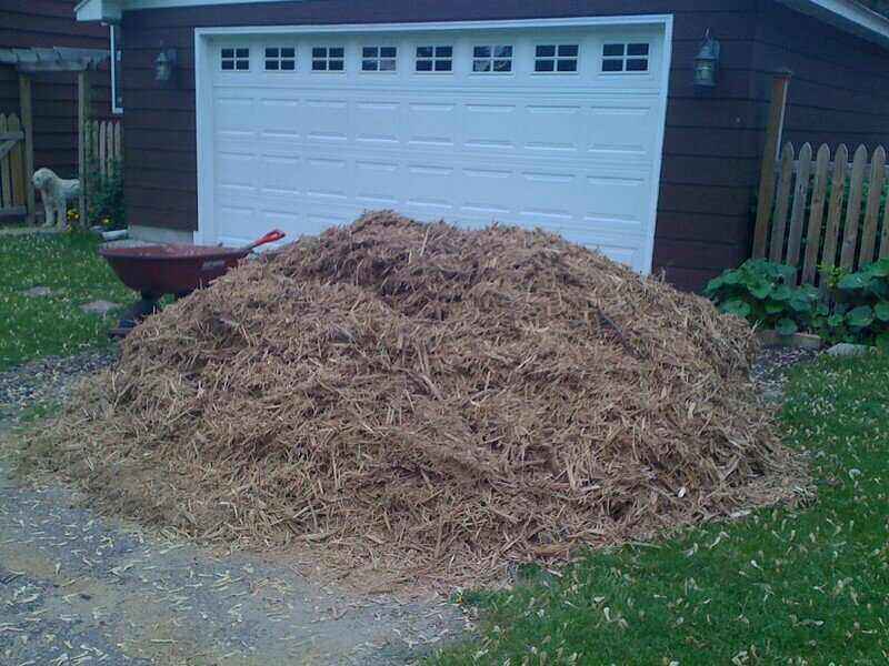 Large pile of mulch in a driveway with a wheel barrow in the background