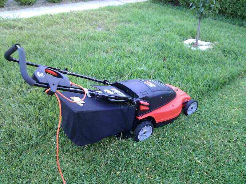 Red electric mower sitting with half the yard mowed