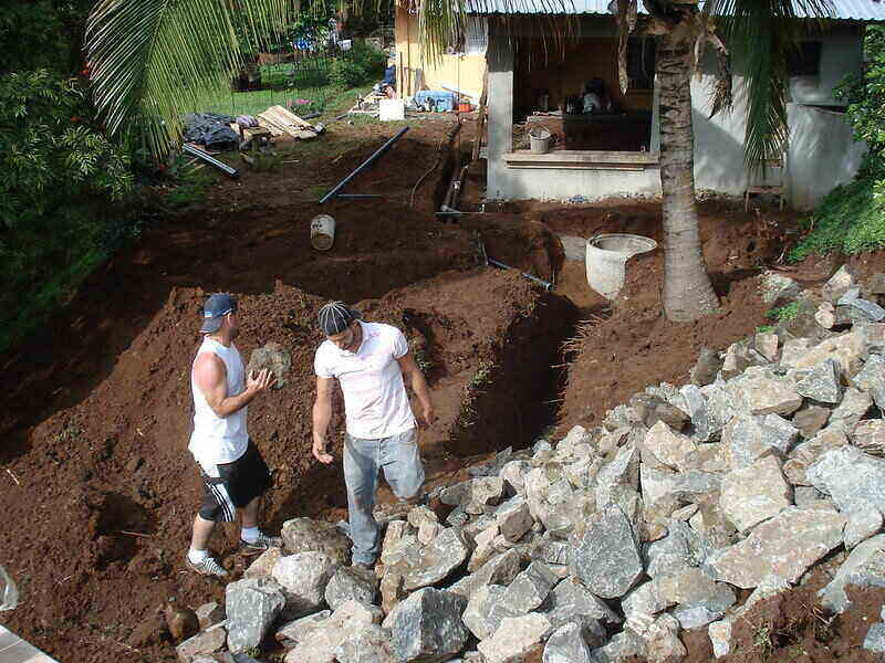 Two men lifting large rocks out of an area to make room for a septic tank