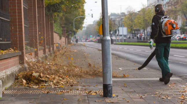 Man blowing leaves off a sidewalk with gas powered leaf blower