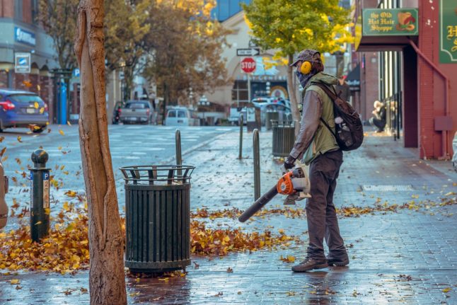 man blowing leaves off sidewalk with leaf blower
