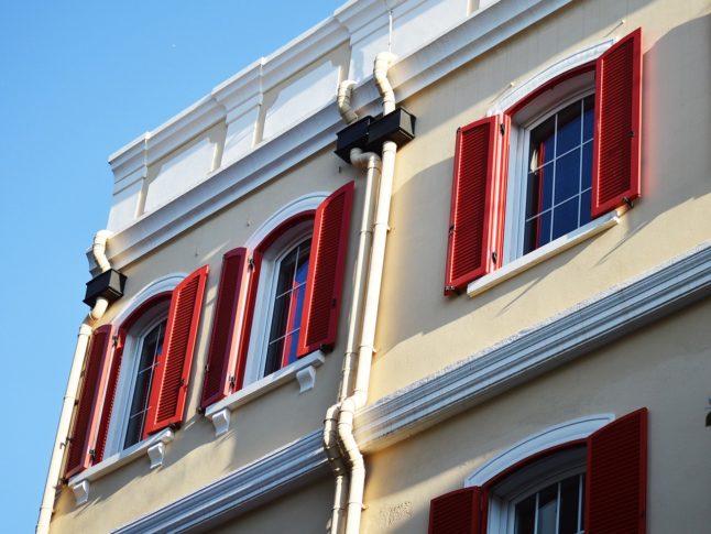 building with red shutters, gutters, and downspouts