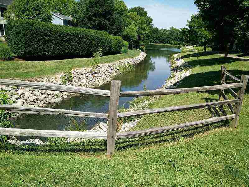 Wooden split rail fence surrounding a stream, with wire mesh covering the bottom of the fence