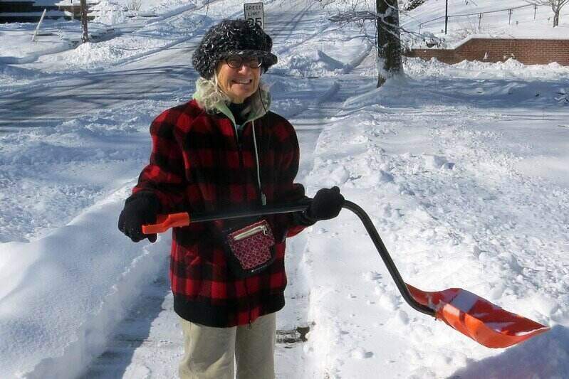 Woman holding a snow shovel while standing on a cleared sidewalk