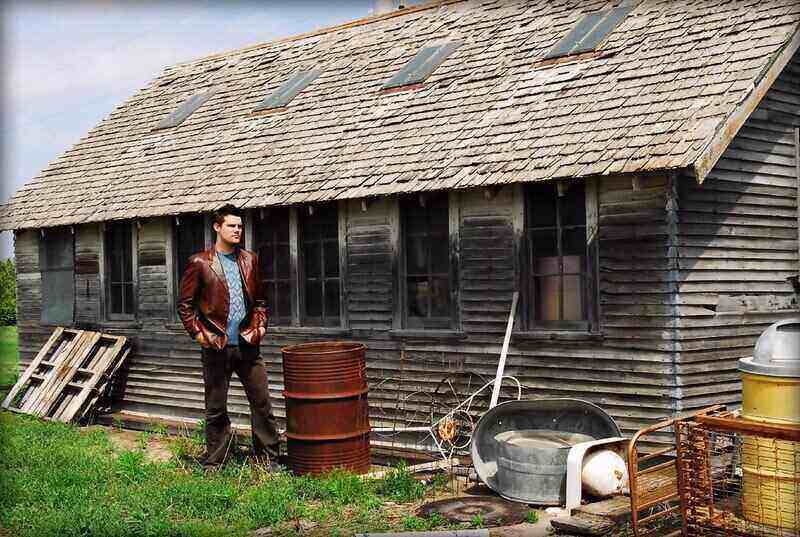 Man standing next to a large wooden shed with many windows along the side