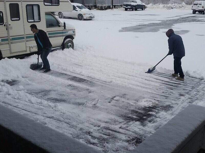 two people shoveling a driveway using snow shovels