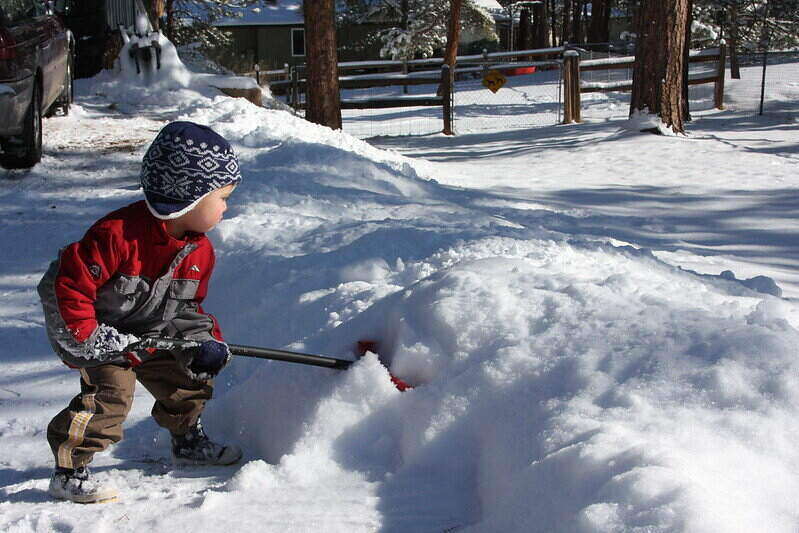 Small child shoveling snow using a snow shovel