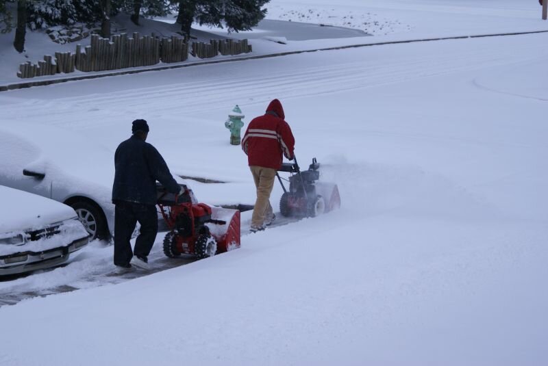 Two people using snow blowers side-by-side