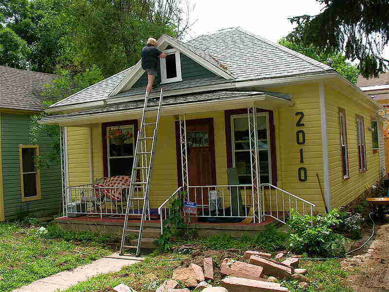 Person standing on a ladder painting the exterior of a house