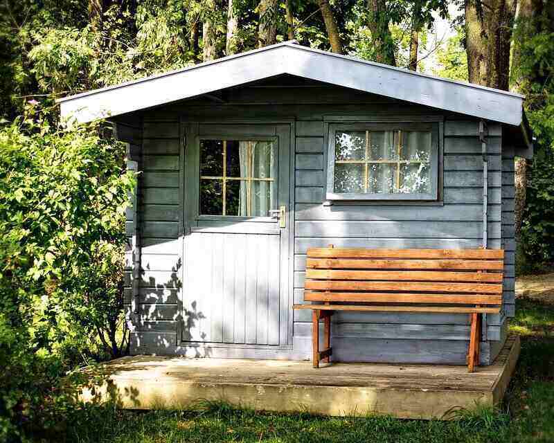 Small cottage style shed with a bench out front on a small porch