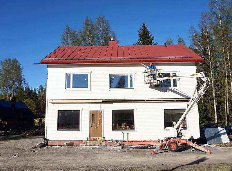 Person painting the top edge of a house using a lift bucket to stand in