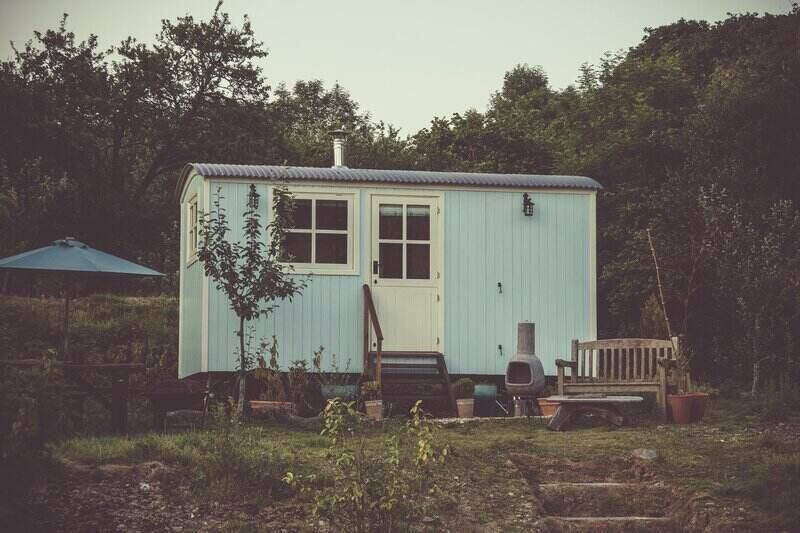 Small metal shed with an chimney and outdoor fire pit with wood bench next to it