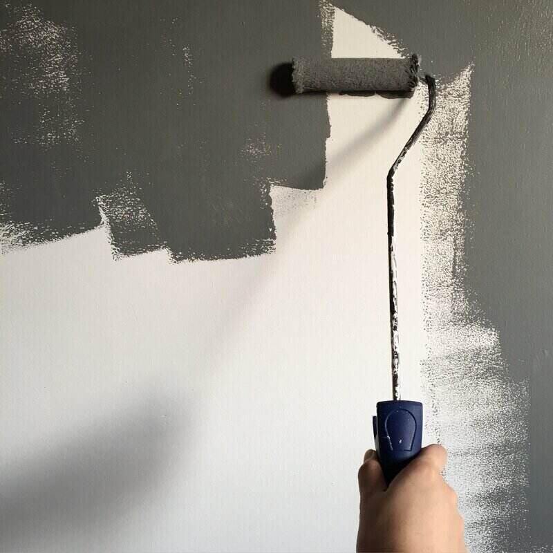 Paint roller on a wall with grey paint