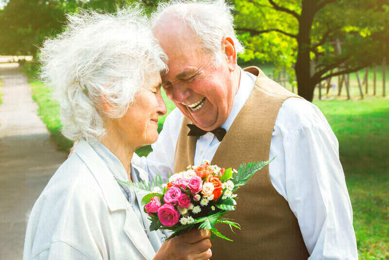 Senior couple laughing together in a park and the woman is holding flowers