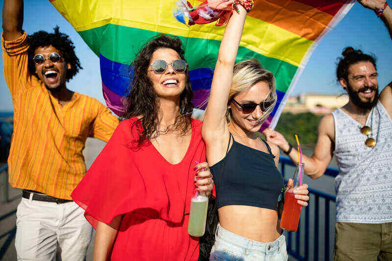 Group of friends attending a gay pride event, while holding a pride flag above their heads