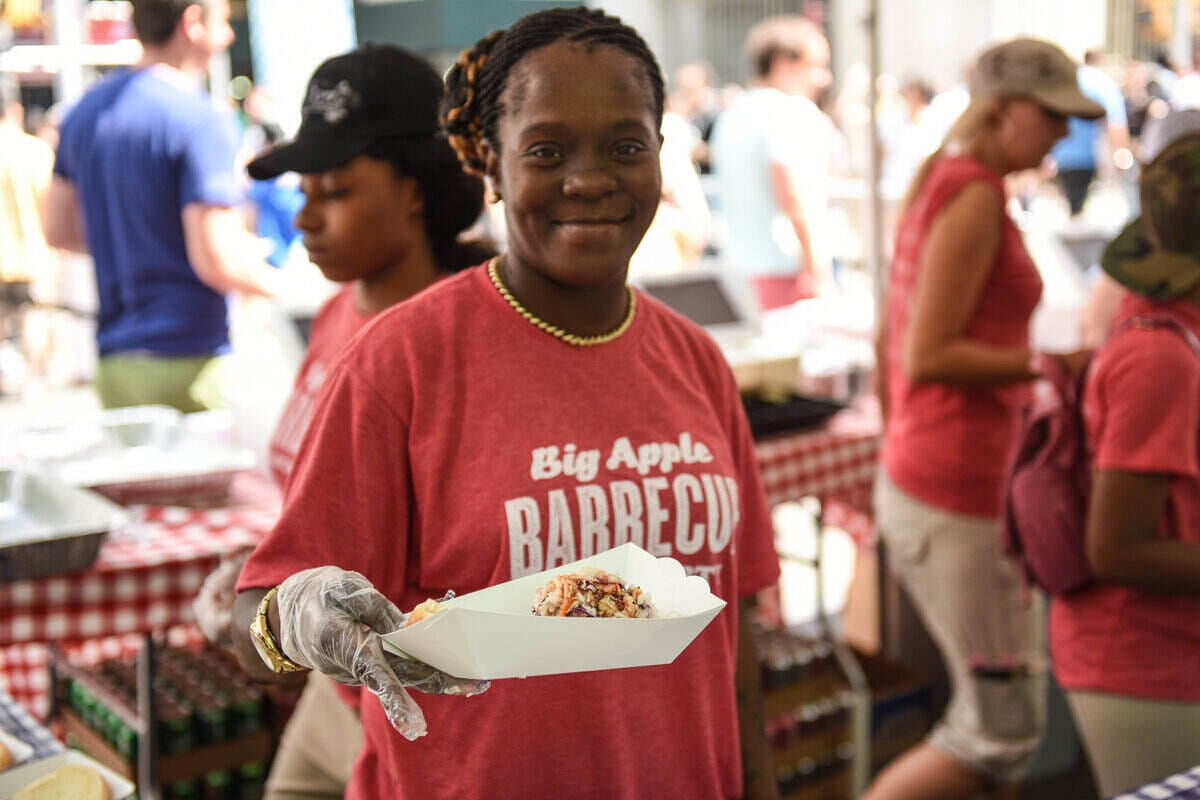 A black woman extends a container of barbecue to a customer at the Big Apple Barbecue Festival.