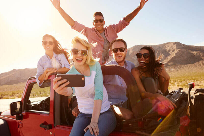 Friends on a road trip in a red Jeep, taking a selfie