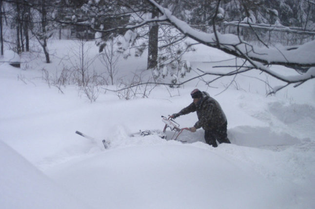 man pushing snow blower through heavy snowfall