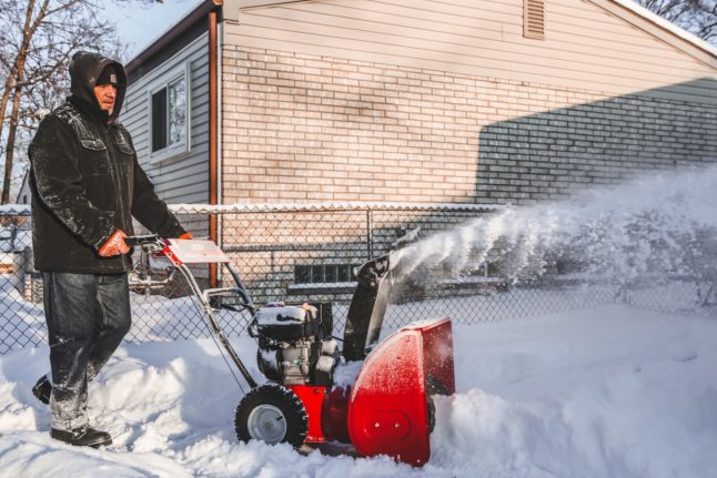 man pushing snowblower through snow in yard